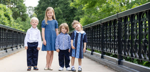 Four children standing on a bridge with greenery in the background