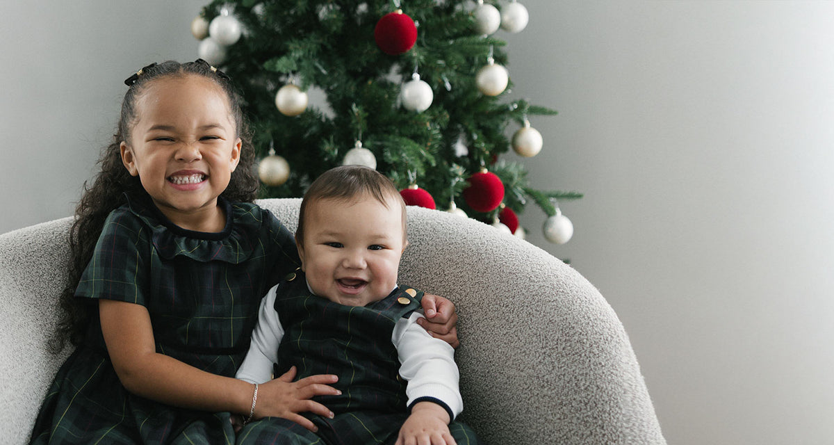 Two children sitting on a couch in front of a decorated Christmas tree.